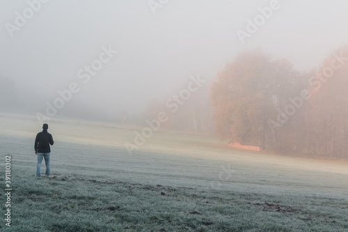 Young man standing on meadow with autumn forest in freeze misty morning fog. Czech landscape