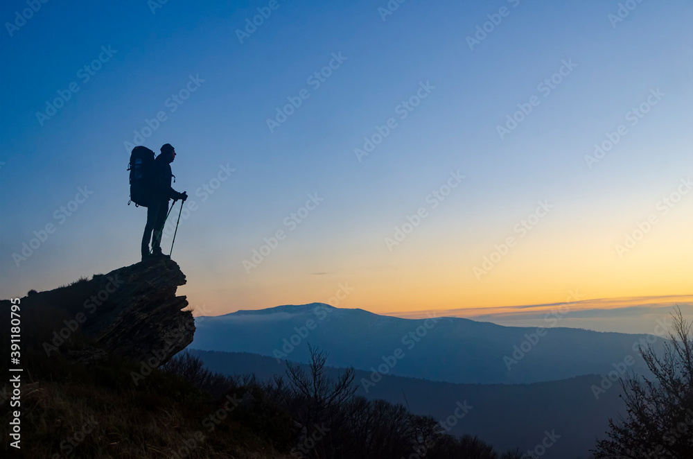 Hiker with backpack on the mountain top enjoys the sunset.