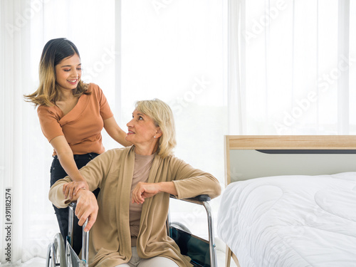 Fotografie Happy mix skin family living together, asian daughter takes care of her  adopted caucasian mother sitting on a wheelchair