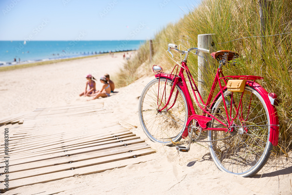 Obraz premium Enfant sur la plage jouant dans le sable à côté d'un vieux vélo rouge abandonné par un vacancier.