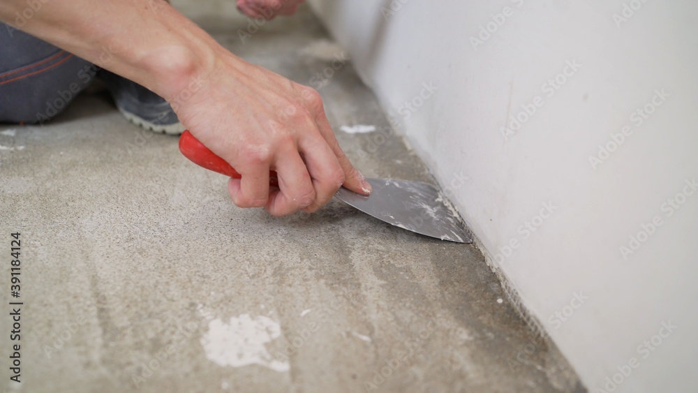 A worker cleans the floor with a spatula, repairs. Close-up of a hand and a spatula. A worker cleans the floor with a spatula. A worker cleans the floor with a spatula, repairs. Close-up of a hand and a spatula. A worker cleans the floor with a spatula.
