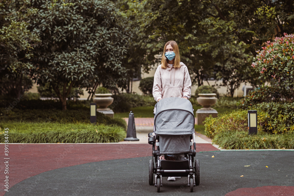 young caucasian mother walking with newborn baby in buggy due to coronavirus covid-19 pandemic lockdown. People wearing face mask for disease prevention. Social distancing. Mom using carriage in park young caucasian mother walking with newborn baby in buggy due to coronavirus covid-19 pandemic lockdown. People wearing face mask for disease prevention. Social distancing. Mom using carriage in park
