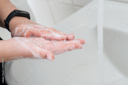 Young adult washing hands with soap in bathroom.