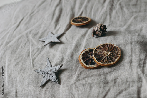 Christmas neutral still life composition. Birch bark stars, larch cones and dry orange slices on grey linen table cloth background. Moody winter design. Selective focus.