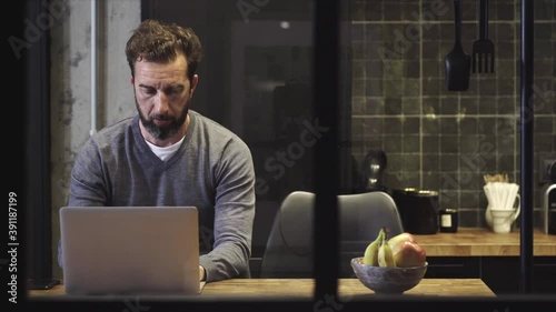 A man works with the computer from the kitchen of his house 