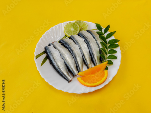 Cleaned and ready to cook fresh indian sardine decorated with curry leaves,lemon slice and tomato slice .Isolated on yellow background. photo