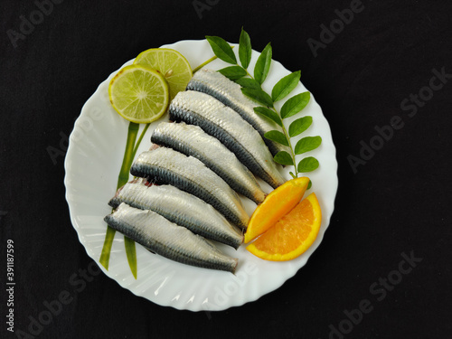 Cleaned and ready to cook fresh indian sardine decorated with curry leaves,lemon slice and tomato slice .Isolated on black background. photo