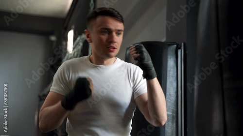 Strong athlete man workingout and training with a punching bag. Male boxer with wrapped hands in the gym. photo
