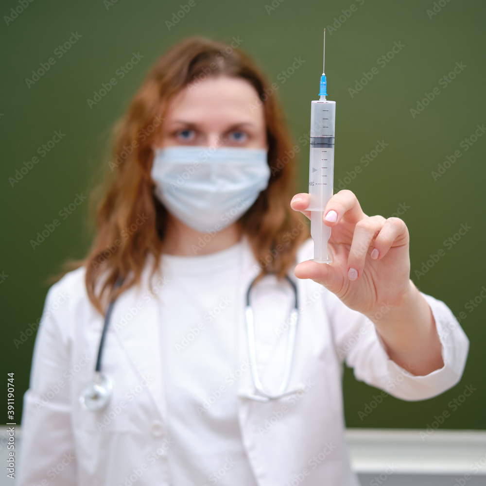 Doctor with a large syringe for vaccination in a school class. The problem with lessons in the classroom during the virus outbreak Doctor with a large syringe for vaccination in a school class. The problem with lessons in the classroom during the virus outbreak