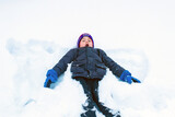 The child is lying on the snow in the pose of a snow angel. Boy on ice in a snow field