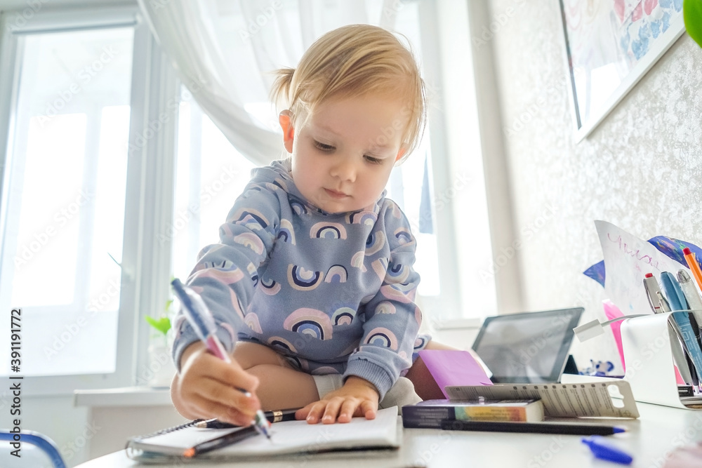 Adorable little girl in beautiful suit painting and sitting on the table. Light and white interior. Adorable little girl in beautiful suit painting and sitting on the table. Light and white interior.