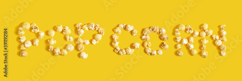 Inscription popcorn on yellow background close-up, top view