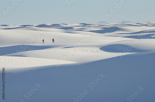 Two people at a distance walking across white sand dunes.
