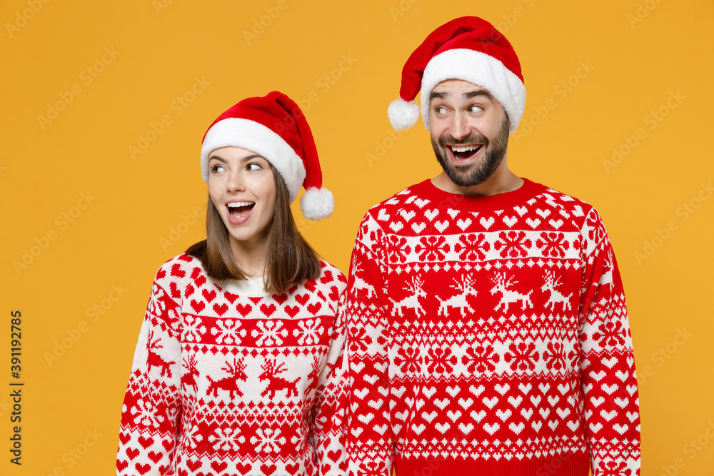 Excited young Santa couple friends man woman in red sweater, Christmas hat keeping mouth open looking aside isolated on yellow background studio portrait. Happy New Year celebration holiday concept. Excited young Santa couple friends man woman in red sweater, Christmas hat keeping mouth open looking aside isolated on yellow background studio portrait. Happy New Year celebration holiday concept.