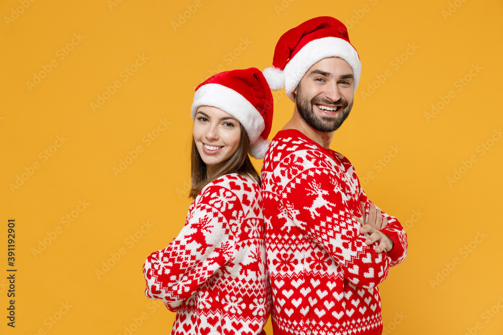 Side view of smiling young Santa couple friends man woman 20s in red sweater Christmas hat holding hands crossed isolated on yellow background studio. Happy New Year celebration merry holiday concept. Side view of smiling young Santa couple friends man woman 20s in red sweater Christmas hat holding hands crossed isolated on yellow background studio. Happy New Year celebration merry holiday concept.