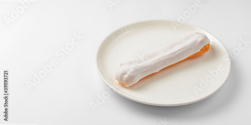 White chocolate eclair on plate on white background. Delicious vanilla dessert for tea time.