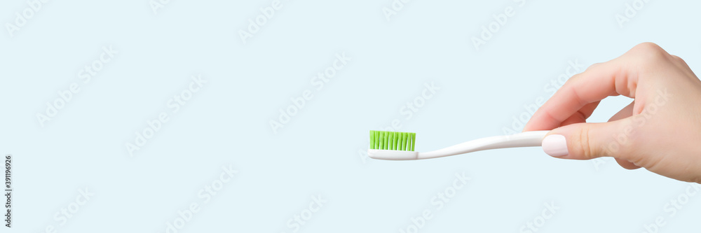 Young adult woman hand holding new white toothbrush with green bristles on light blue background. Pastel color. Teeth hygiene concept. Closeup. Empty place for text or logo. Dental banner. Young adult woman hand holding new white toothbrush with green bristles on light blue background. Pastel color. Teeth hygiene concept. Closeup. Empty place for text or logo. Dental banner.