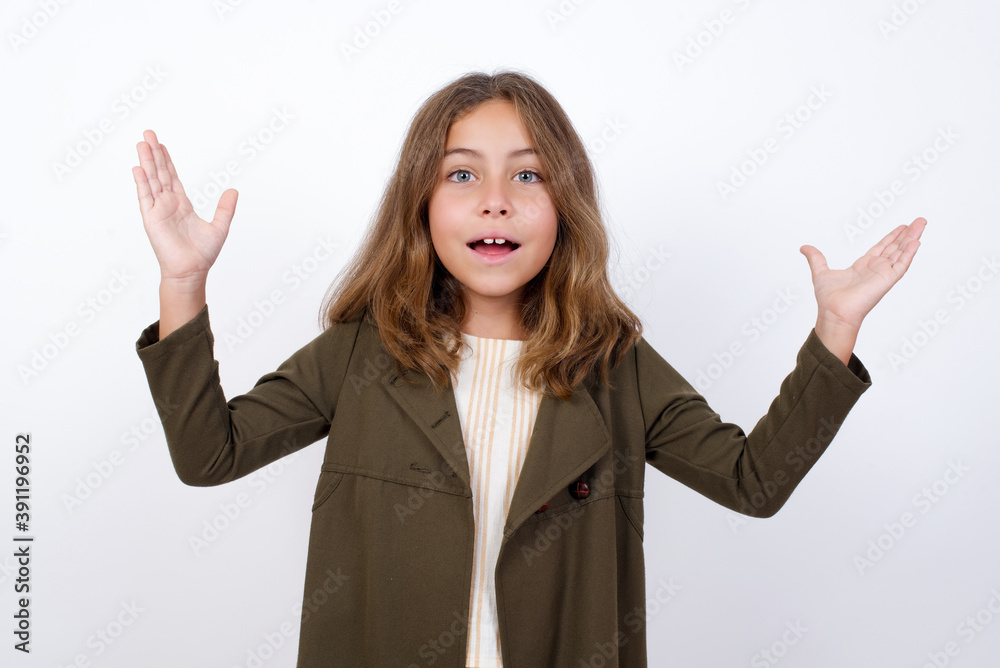 Beautiful little girl standing against white background, raising hands up, having eyes full of happiness rejoicing his great achievements. Achievement, success concept. Beautiful little girl standing against white background, raising hands up, having eyes full of happiness rejoicing his great achievements. Achievement, success concept.