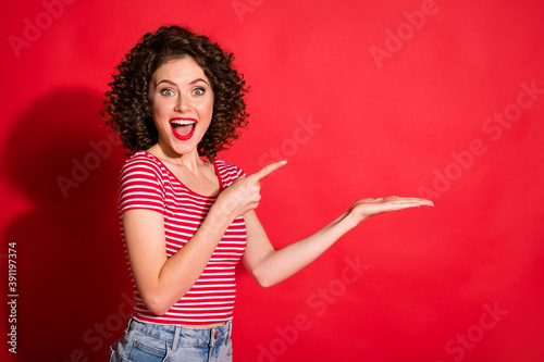 Photo of surprised wavy young woman dressed striped outfit pointing empty space demonstrating product isolated red color background