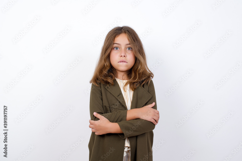 Beautiful little girl standing against white background, bitting his mouth and looking worried and scared crossing arms, worry and doubt. Beautiful little girl standing against white background, bitting his mouth and looking worried and scared crossing arms, worry and doubt.