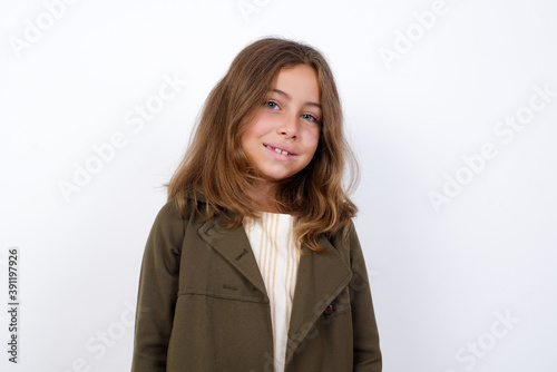 Charming Beautiful little girl standing against white background, feeling shy, smiling and looking to the camera.