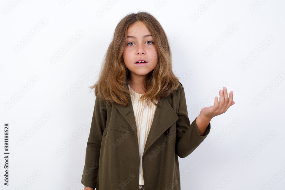 Studio shot of frustrated Beautiful little girl standing against white background, gesturing with raised palm, frowning, being displeased and confused with dumb question. Studio shot of frustrated Beautiful little girl standing against white background, gesturing with raised palm, frowning, being displeased and confused with dumb question.