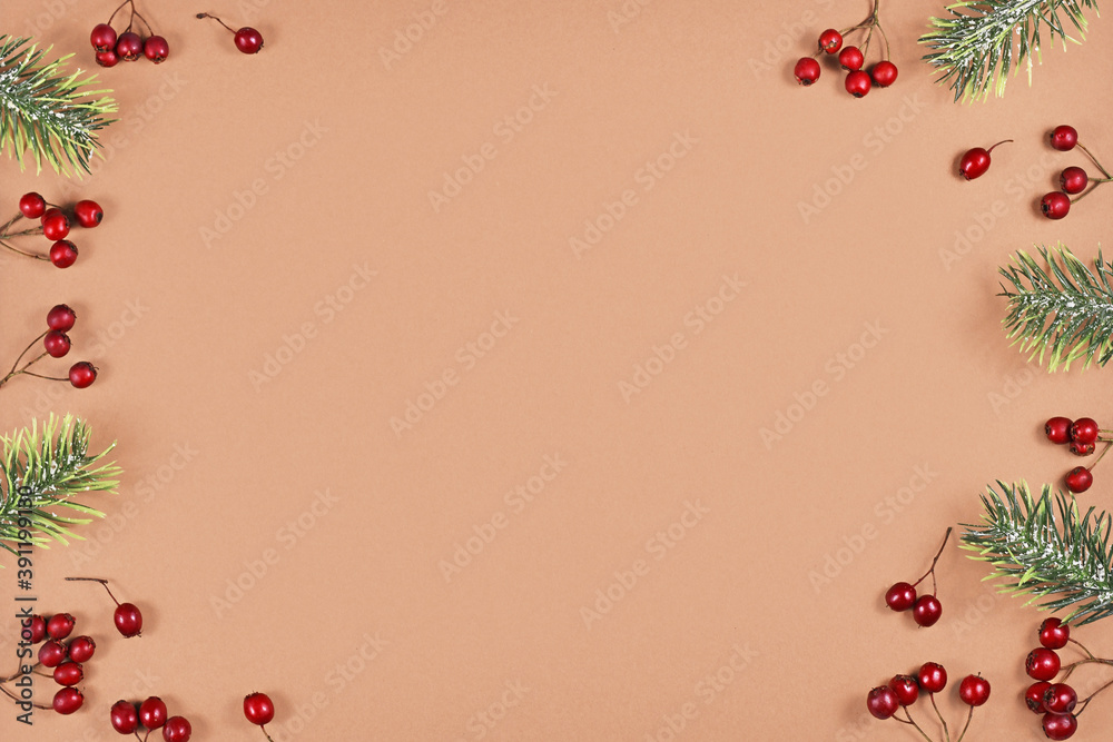 Festive winter flat lay with red berries and fir tree branches forming border around brown background with empty copy space