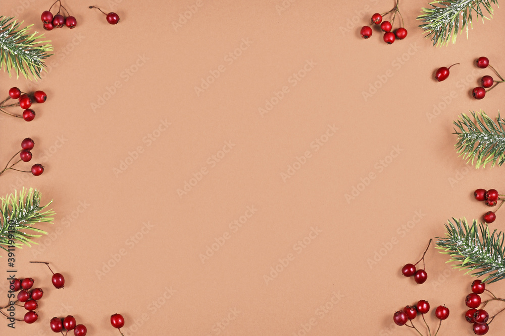 Festive winter flat lay with red berries and fir tree branches forming border around brown background with empty copy space Festive winter flat lay with red berries and fir tree branches forming border around brown background with empty copy space