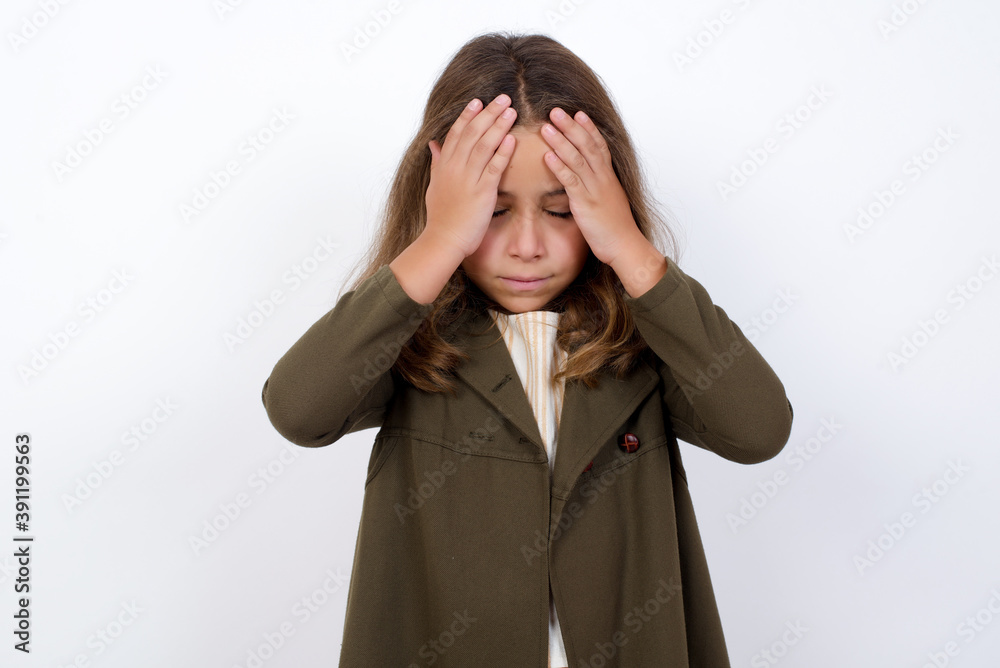 Beautiful little girl standing against white background, holding head with hands, suffering from severe headache, pressing fingers to temples Beautiful little girl standing against white background, holding head with hands, suffering from severe headache, pressing fingers to temples