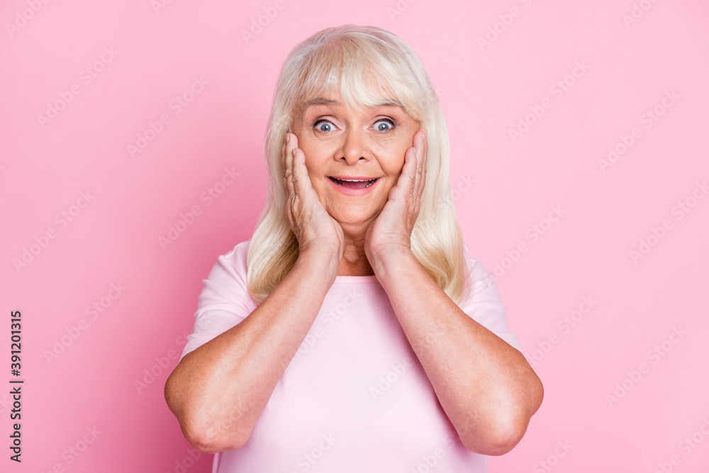 Photo portrait of amazed smiling grandmother touching cheeks staring isolated on pastel pink color background