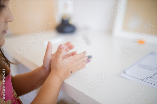 Little girl putting her hands with paint stains together above a white desk