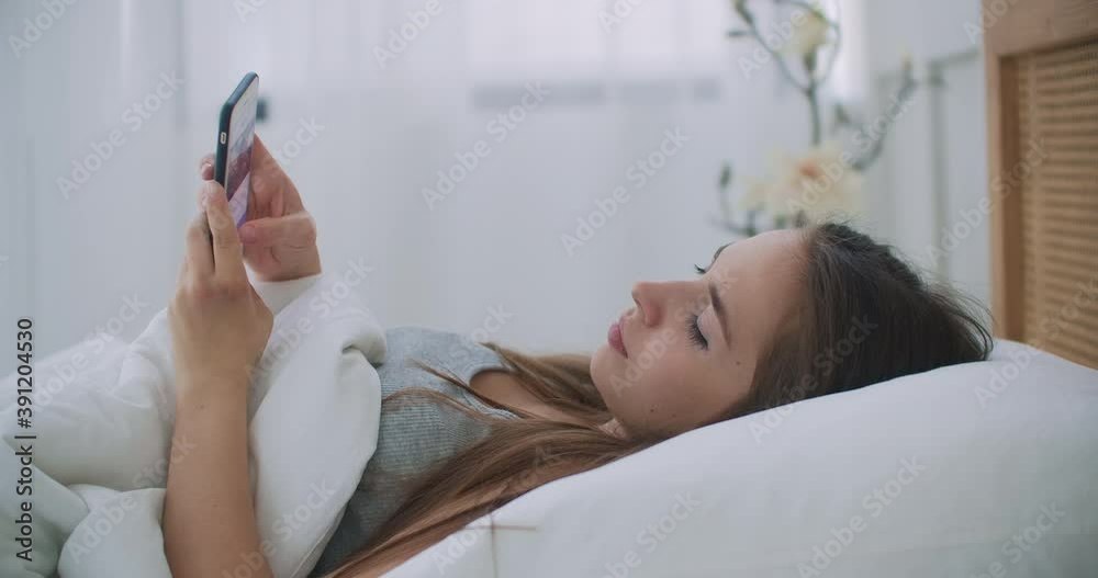 Woman holding mobile phone while lying in bed at home. Woman holding mobile phone while lying in bed at home.