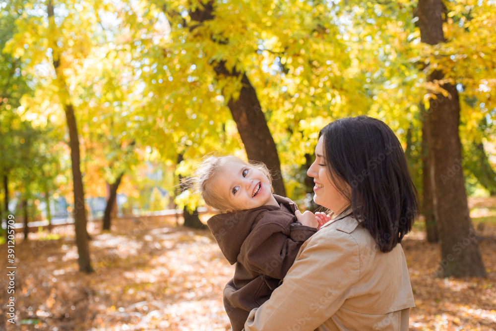 A young mother and little daughter are walking and laughing in the autumn park. Family. Autumn mood A young mother and little daughter are walking and laughing in the autumn park. Family. Autumn mood