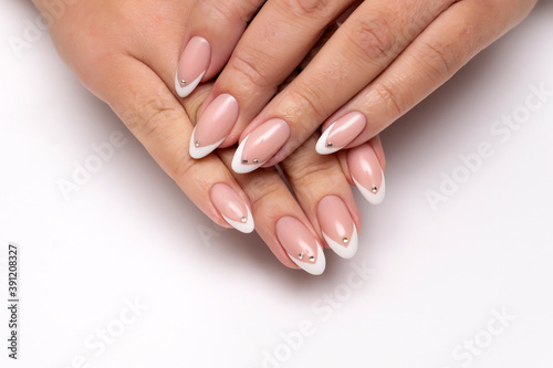 Gel manicure with crystals  stones on all nails. French white sharp manicure on long sharp nails close-up on a white background.