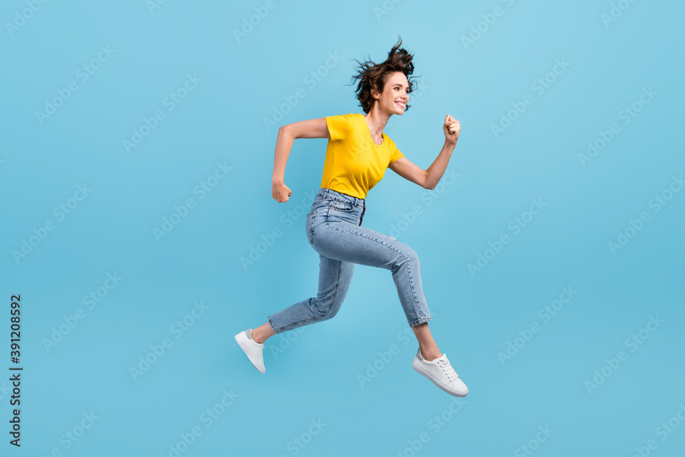 Full length profile photo of young lady jump run wear yellow t-shirt jeans sneakers isolated blue color background
