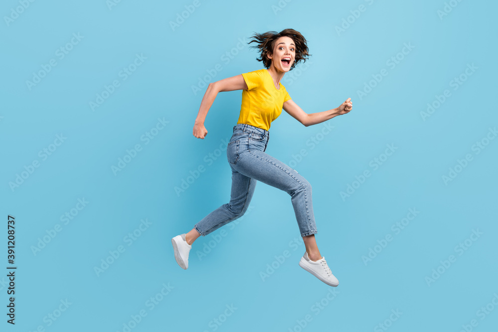Full length profile photo of excited girl jump run open mouth wear yellow t-shirt jeans footwear isolated blue color background