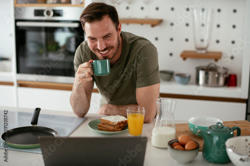 Young man eating breakfast and reading the news online. Handsome man enjoying at home.