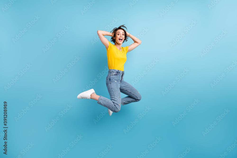 Full length photo of funny lady jump arms head open mouth wear yellow t-shirt jeans sneakers isolated blue color background Full length photo of funny lady jump arms head open mouth wear yellow t-shirt jeans sneakers isolated blue color background