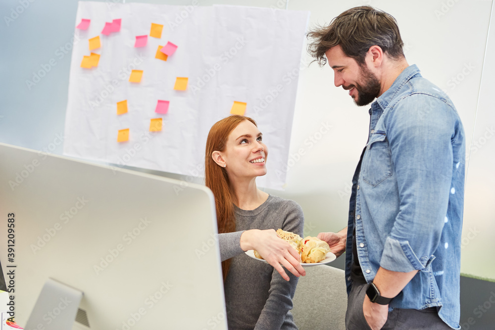 Mann bringt einer Kollegin einen Teller mit Snacks Stock Photo