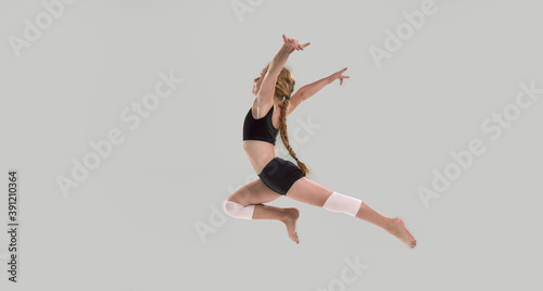 Full length shot of cute little redhead girl, professional gymnast jumping isolated over grey background