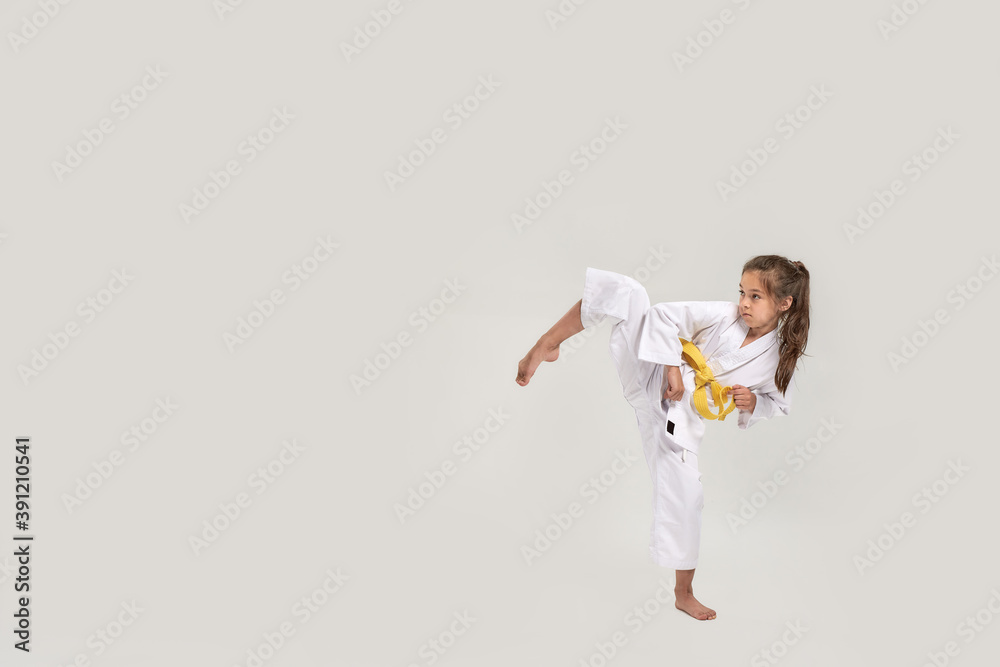 Full length shot of little karate girl in white kimono with a yellow sash exercising and fighting, doing martial arts, standing isolated over white background Full length shot of little karate girl in white kimono with a yellow sash exercising and fighting, doing martial arts, standing isolated over white background