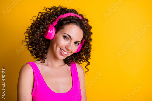 Closeup photo of attractive youngster wavy lady listen modern ear flaps overjoyed new gadget coquettish eyes look wear pink tank top singlet isolated vibrant shine yellow color background