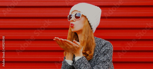 portrait of young woman blowing red lips sending sweet air kiss over red background © rohappy