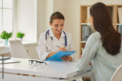 Friendly doctor with clipboard writing down patient's personal information in modern hospital office