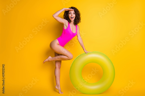 Full length photo of pretty funny tourist lady swim big green round float circle look distant wondered ship cruise landscapes wear pink swimsuit isolated vivid yellow color background