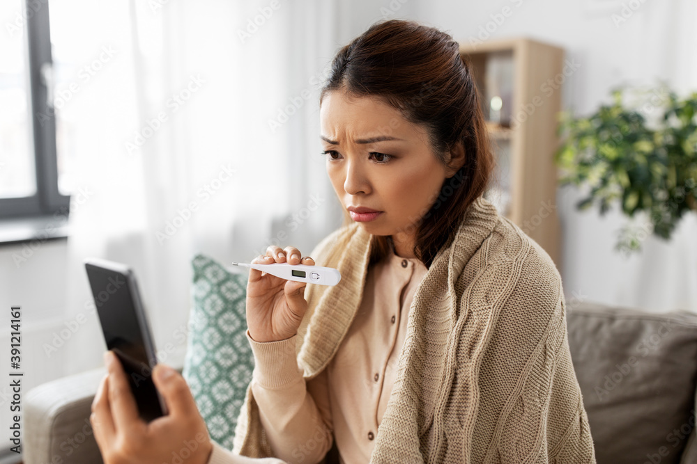 healthcare, technology and people concept - sick asian woman in blanket with thermometer having video call on smartphone at home healthcare, technology and people concept - sick asian woman in blanket with thermometer having video call on smartphone at home