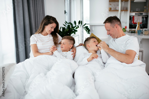 Young family enjoying in bed. Happy parents with sons relaxing in bed...