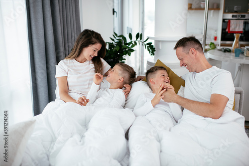 Young family enjoying in bed. Happy parents with sons relaxing in bed...