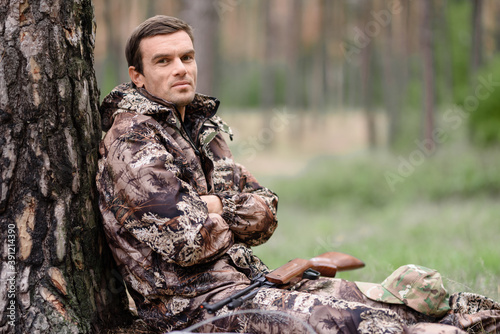 Lonely Hunter in Camo Has Rest Sitting under Tree.