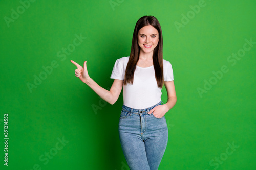Photo of confident girl wear casual outfit pointing one finger looking empty space arm pocket isolated green color background